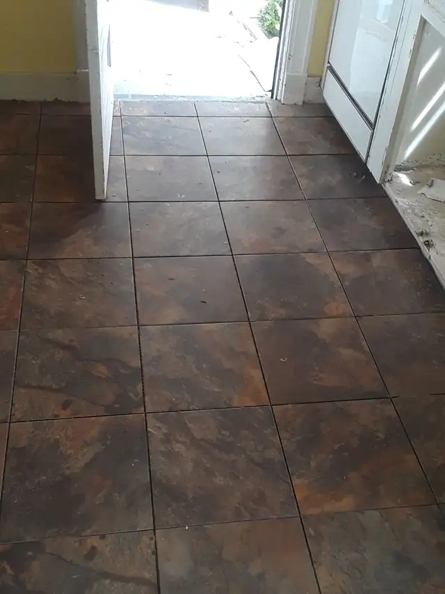 Rust and brown slate-look square floor tiles set through a back entry, before grouting